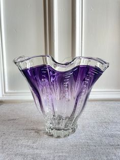 a purple glass vase sitting on top of a table next to a white wall and carpet