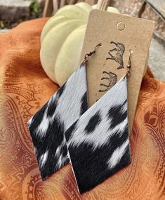 black and white cow print earrings on top of an orange cloth with pumpkins in the background