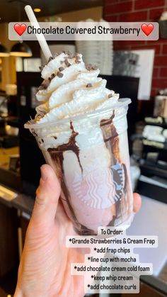 a person holding up a cup with whipped cream and chocolate toppings on it in front of a counter