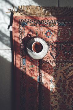 a cup of coffee sitting on top of a table next to a rug with an intricate design