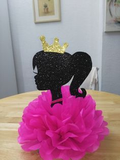 there is a cake topper with a crown on it and a pink flower in front of it