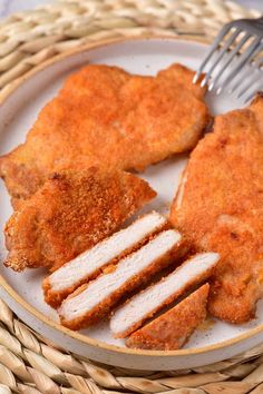 a white plate topped with chicken cutlets and two slices of breaded meat next to a fork