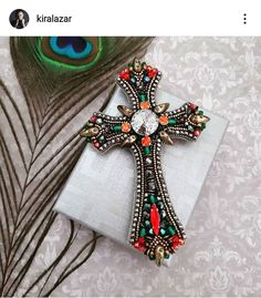 a cross brooch sitting on top of a piece of cloth next to a peacock feather