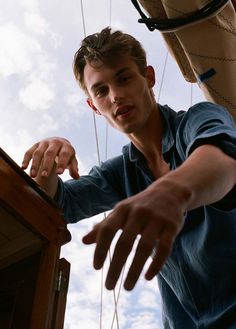 a man standing on top of a boat next to a tall wooden structure with ropes hanging from it's sides