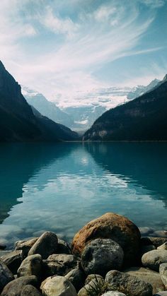 a lake surrounded by mountains and rocks under a cloudy sky