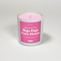 a pink candle is sitting in a white container on a gray surface with the words mojo dojo casa mouse written below it