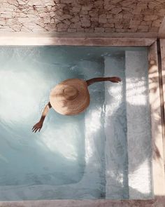 a person wearing a straw hat floating in a pool with blue water and stone walls