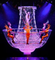 a group of women on stage performing in front of a large boat with lights and decorations