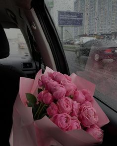 a bouquet of pink roses sitting in the back seat of a car on a rainy day