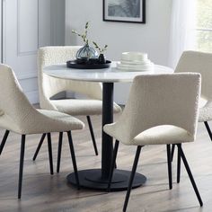 a white table with four chairs around it and a vase on the table next to it