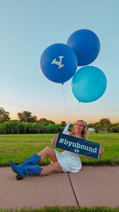 a woman sitting on the ground with balloons in front of her and holding a sign