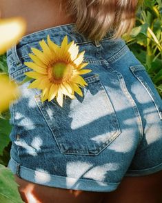 the back of a woman's jean shorts with a sunflower pinned to it