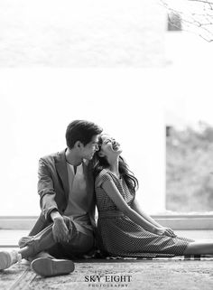 a man and woman sitting next to each other on the floor in front of a window