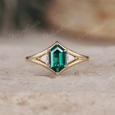 an emerald and diamond ring sitting on top of a table