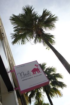 a sign hanging from the side of a tall building next to palm trees and a sky background