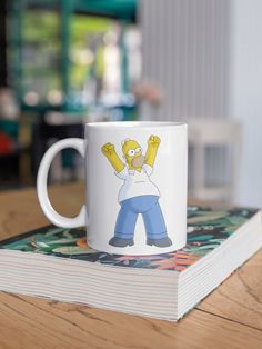 a white coffee mug with the simpsons character on it sitting on top of a book