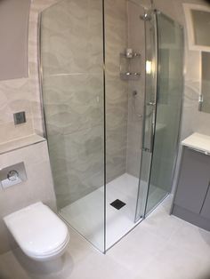 a white toilet sitting next to a walk in shower and a glass enclosed shower stall