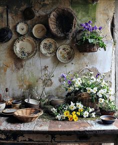 an old table topped with lots of plates and bowls filled with flowers in front of a wall