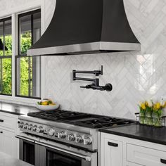 a kitchen with white cabinets and black counter tops, an oven hood over the stove