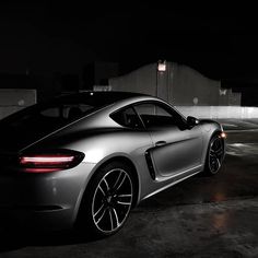 a silver sports car parked in a parking lot with its lights on at night time