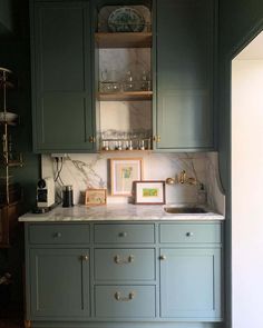 a kitchen with green cabinets and marble counter tops, gold pulls on the cupboards