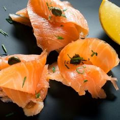 four pieces of raw salmon on a black plate with lemon wedges and seasoning