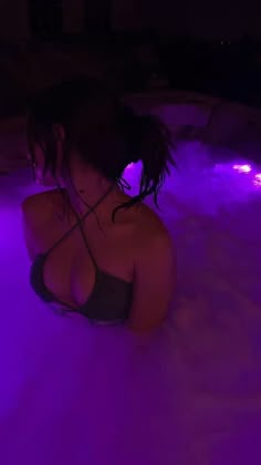 a woman is sitting in the hot tub with purple lights on her face and hair