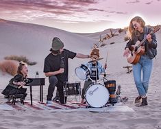 a group of people that are playing some music on the beach with sand dunes in the background