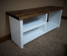 a white entertainment center with wooden top and shelves on carpeted floor next to wall