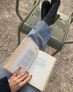 a person sitting on a bench reading a book with their feet propped up in the air