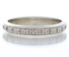 an antique wedding band with flowers and leaves in white gold, set on a plain surface