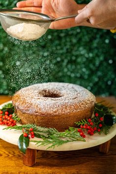 someone is sprinkling sugar on a bundt cake with holly and red berries