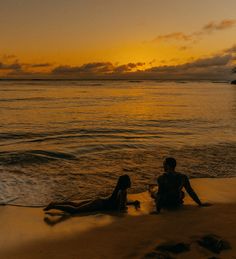 two people are sitting on the beach at sunset