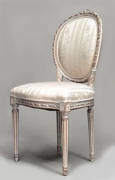 an antique chair with white upholstered fabric and silver trimming on the back