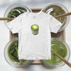 a cupcake t - shirt sitting on top of some green smoothies in plastic cups