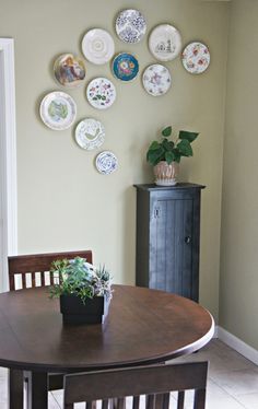 a dining room table with plates on the wall and a potted plant next to it