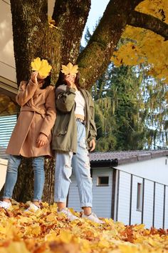 two women standing next to each other in front of a tree with leaves on it