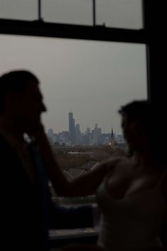 a man and woman standing in front of a window looking out at the city skyline