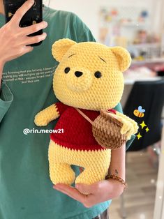 a person holding a cell phone up to their face while wearing a knitted winnie the pooh costume