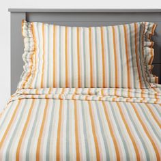 an orange and blue striped bed spread with ruffles on the bottom, in front of a gray headboard