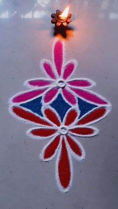 a small candle is lit on the ground in front of a flower design that looks like it has been made out of sand