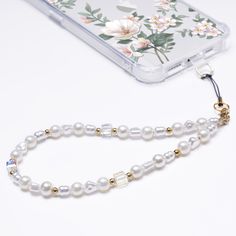 a cell phone with a white beaded necklace on it's side next to a flowered case