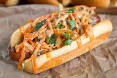 a hot dog covered in toppings sitting on top of a paper wrapper next to some buns