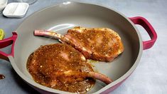 two pork chops are being cooked in a frying pan on a table with utensils