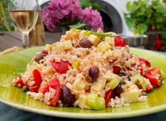 a green plate topped with rice and veggies next to a glass of wine