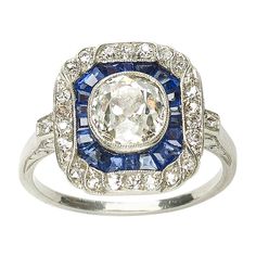 An Art Deco sapphire and diamond ring, with a central old cut diamond, weighing an estimated 1.30ct, in our opinion the colour is I and our opinion of the clarity is VS, in a millegrain edged rub over setting, surrounded by calibré-cut sapphires, with an eight-cut diamond set border and shoulders, with millegrain edges, a pierced gallery and scroll engraved shoulder sides, mounted in platinum. Finger size K ½ UK, 5 3/8 US. Antique Engagement Rings Sapphire, Diamond And Sapphire Ring, Sapphire Cocktail Ring, Vintage Cocktail Ring, Platinum Diamond Rings, Platinum Jewelry, Diamond Cocktail Rings, Fancy Diamonds, Filigree Ring