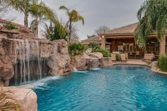 an outdoor pool with waterfall and seating area next to it, surrounded by palm trees