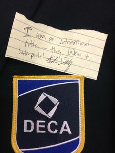 a piece of paper with writing on it next to a deca badge and note