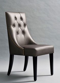 a silver chair with black legs and buttons on the back is in front of a gray wall