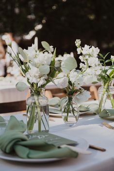 two vases filled with white flowers sitting on top of a table next to plates